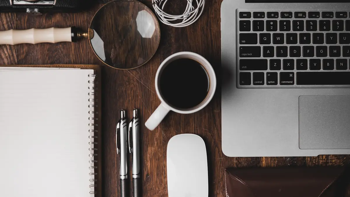 Schreibtisch mit Laptop, Notizbuch und Kaffee – KI-Werkzeuge im Büroalltag